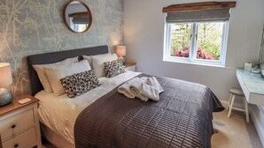 A bedroom with a bed, bedside tables, a mirror, a window with a view of trees, and a desk with a chair. - Haystacks (Windermere)