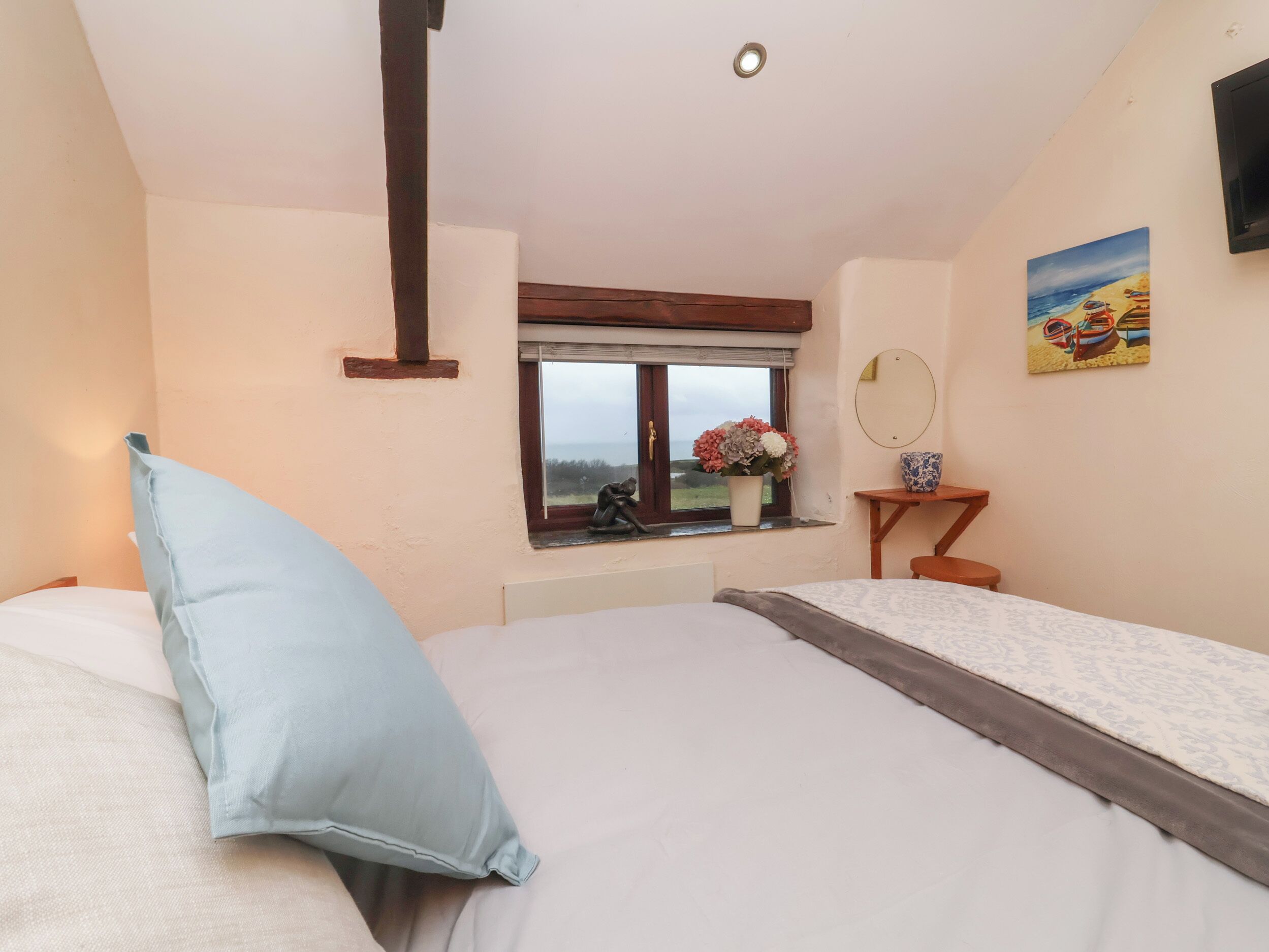 A bedroom with a bed, a window with a view, a small table with a vase, and a painting on the wall.