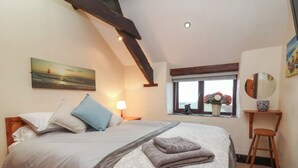 A bedroom with a bed, a nightstand, a window with a view, a mirror, and a small stool. - Badgers Sett (Bude)
