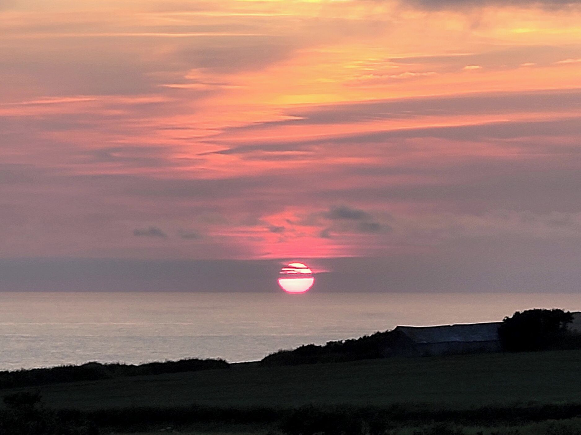 A sunset over a body of water with a silhouette of a building in the foreground.