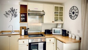 Una cucina compatta con fornello, microonde, lavello e pensili.