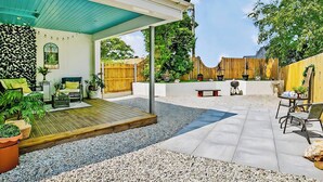 A covered patio area with a wooden deck, seating, and potted plants. - The Studio (Bude)