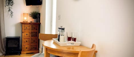 A cozy room with a wooden table, two chairs, a television on the wall, a small cabinet, and a window.
