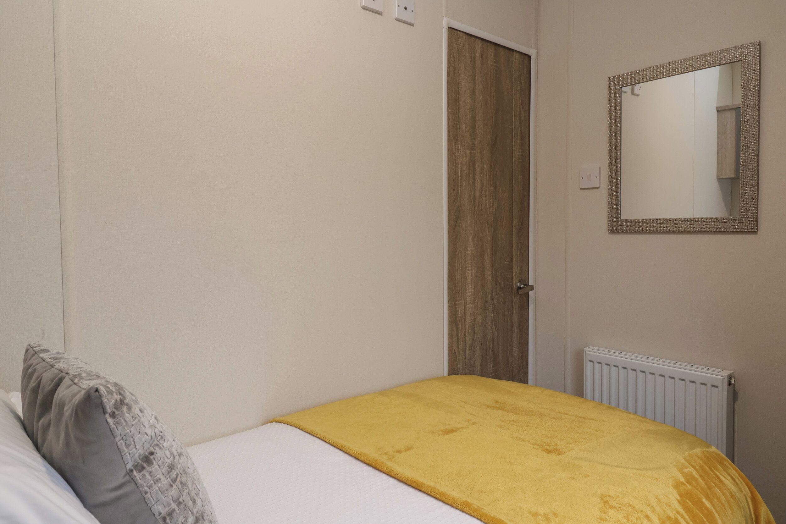 Une chambre à coucher avec un lit, une porte en bois, un miroir et un radiateur.