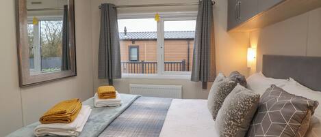 A hotel room with a bed, a window with curtains, a radiator, and a view of a building outside.