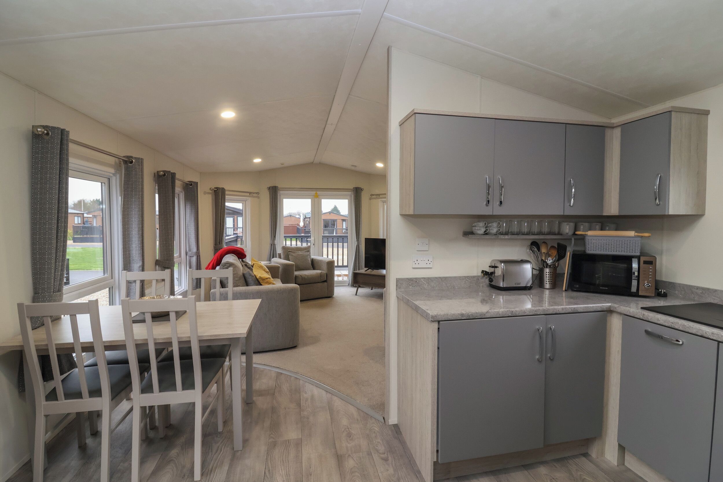 A modern kitchen with grey cabinets, a microwave, toaster, and a sink. There is a dining area with a table and chairs.