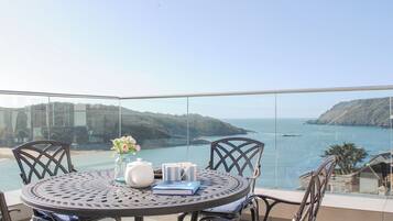 A round metal table with chairs on a balcony overlooking a coastal view.