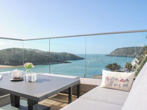 Un balcón con una mesa, un jarrón con flores y vista al mar y las colinas.