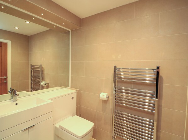 A modern bathroom with a sink, mirror, toilet, and a towel rack.