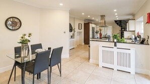 A modern kitchen with a central island, a dining area with a glass table and chairs, and a staircase leading to an upper level. - Hardy's Way 34 (Canvey Island)