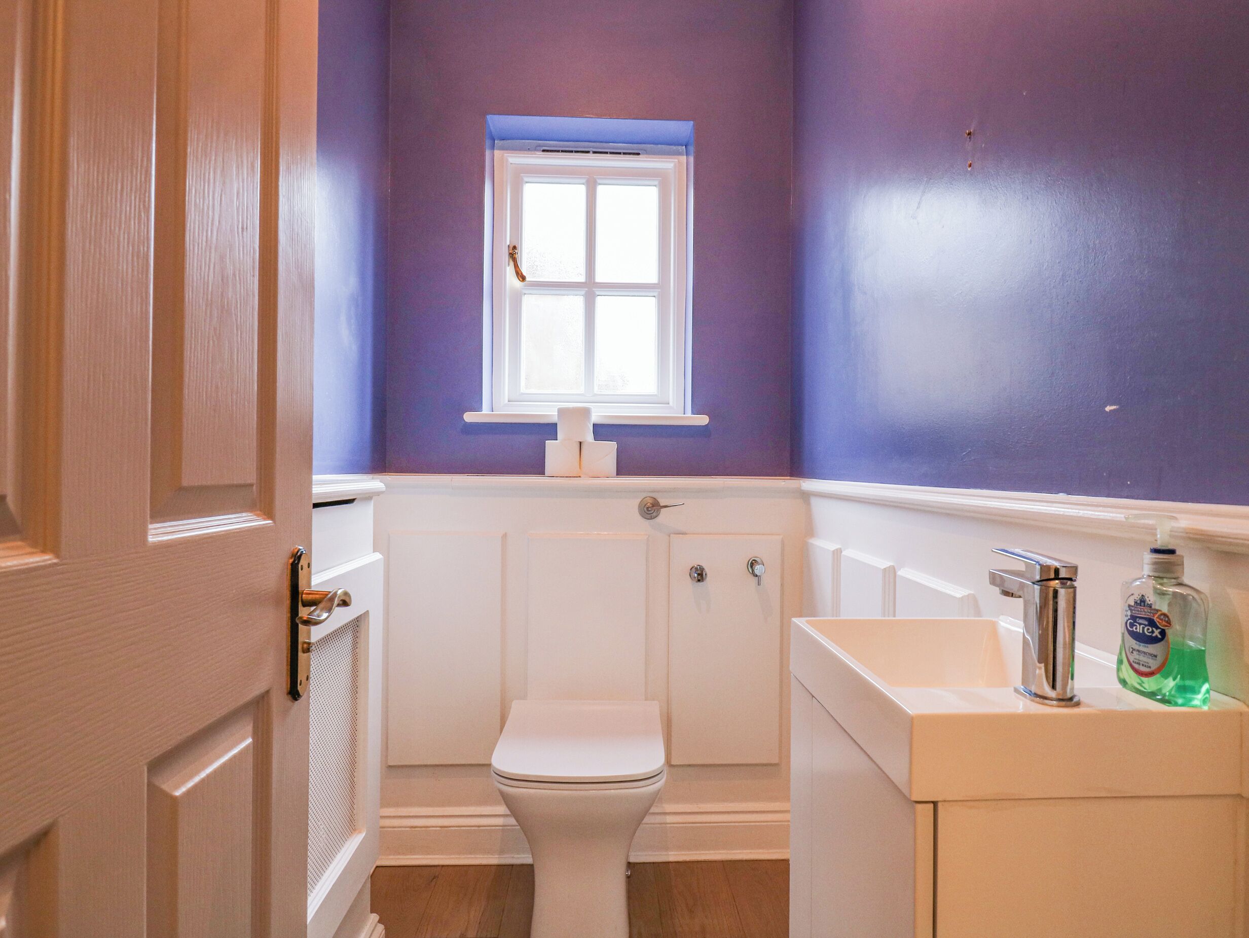 A bathroom with a white toilet, a window above it, and a sink with a soap dispenser.