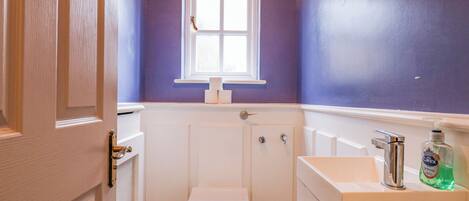 A bathroom with a white toilet, a window above it, and a sink with a soap dispenser.