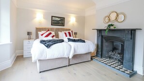 A bedroom with a bed, bedside tables, a fireplace, and a framed picture on the wall. - Hardy's Way 34 (Canvey Island)