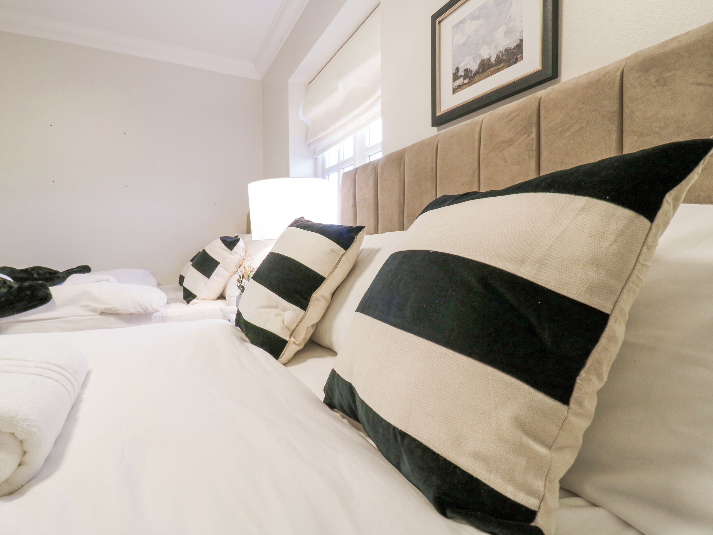 Habitación de hotel con una cama bien hecha, cabecero y un cuadro enmarcado en la pared.