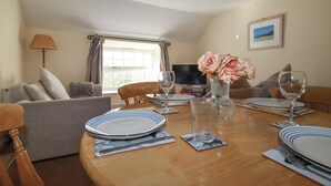 Un comedor con una mesa de madera dispuesta para dos personas, un florero con flores y un televisor al fondo.