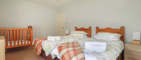 A bedroom with two beds, a crib, a bedside table with a lamp, and a door.