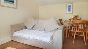 Una sala de estar acogedora con un sofá color beige, una manta blanca y una mesa de comedor con sillas.