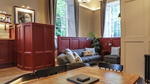 A cozy living room with a wooden dining table, a grey sofa with floral cushions, and a red cabinet. - The Court (Carnforth)