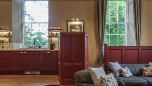 A living room with a dark grey sofa, a wooden coffee table, and a red cabinet. There is a window with curtains and a view of greenery outside. - The Court (Carnforth)