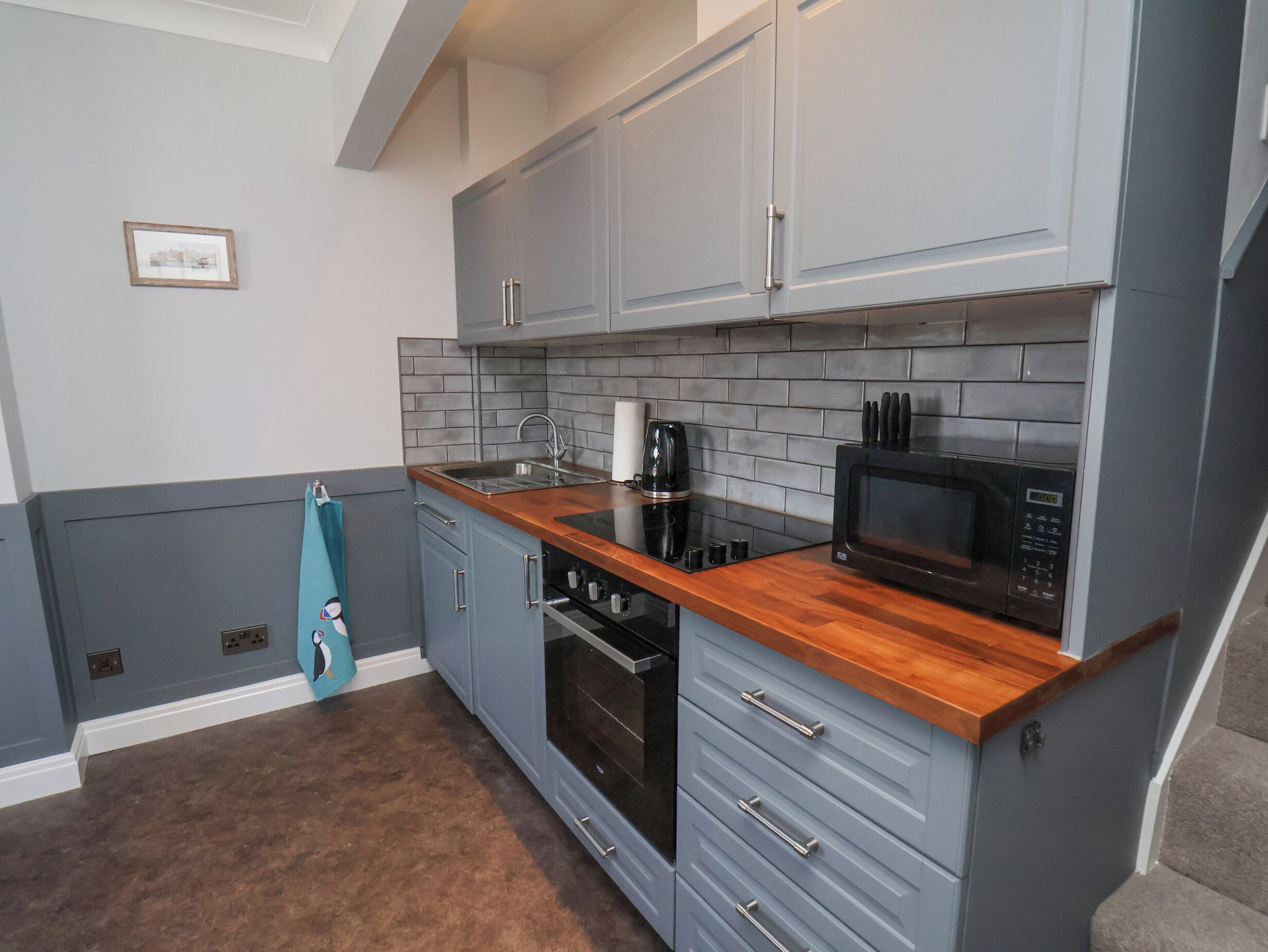 A compact kitchen with grey cabinets, a wooden countertop, a black microwave, and a built-in oven.
