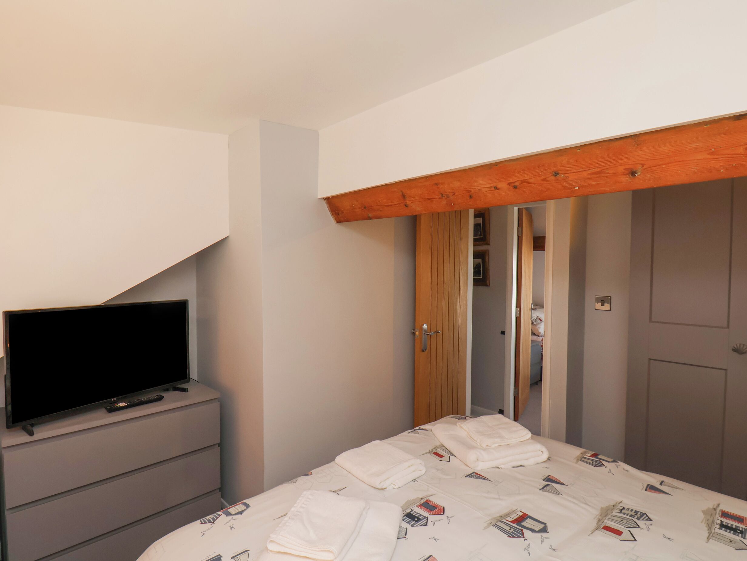 A bedroom with a bed, a TV on a dresser, and a wooden ceiling beam.