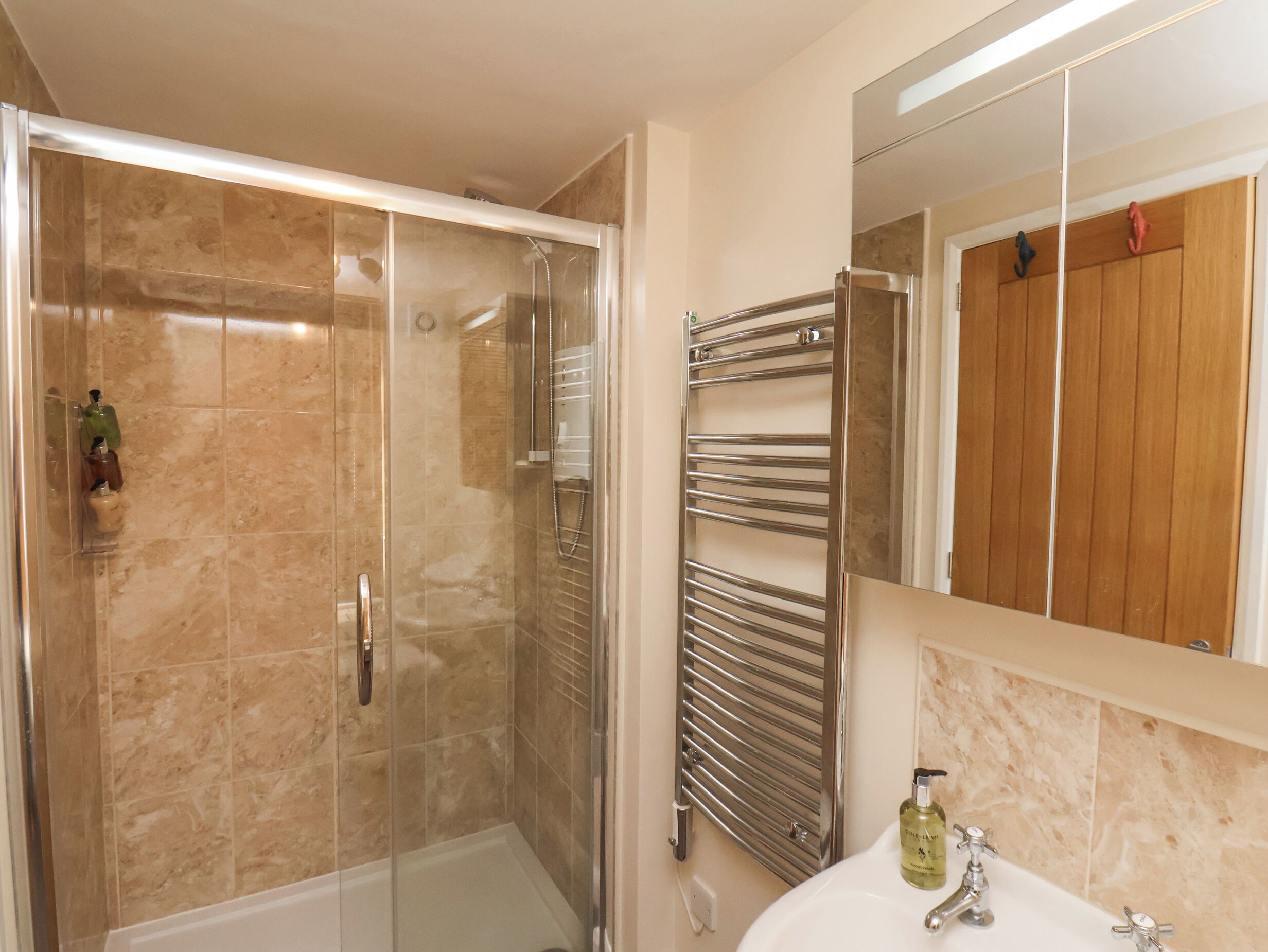 Une salle de bain dotée d’une douche à parois de verre, d’un porte-serviettes chromé, d’une porte en bois et d’un lavabo blanc avec un seul robinet.