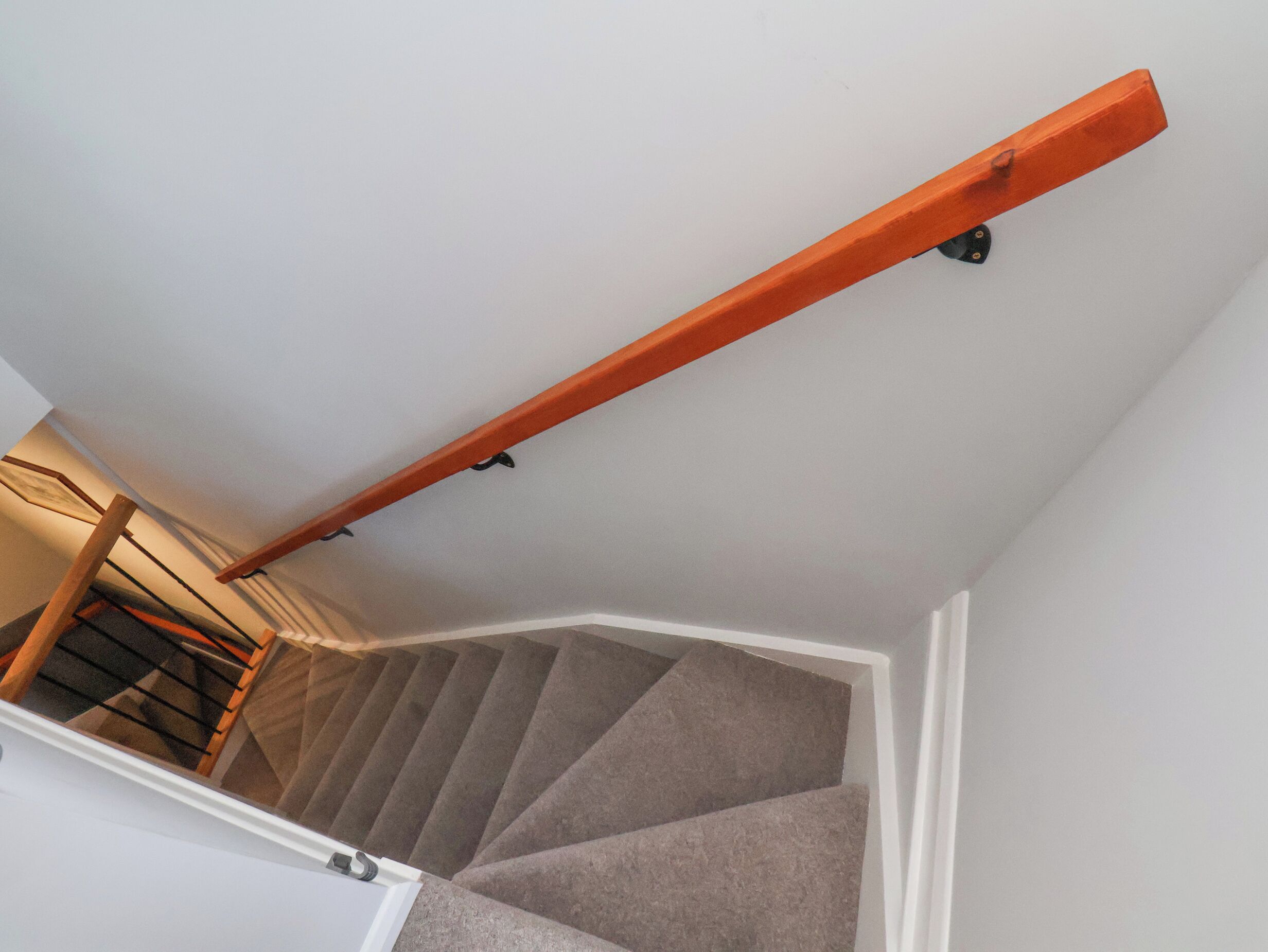 A staircase with a wooden handrail and carpeted steps.