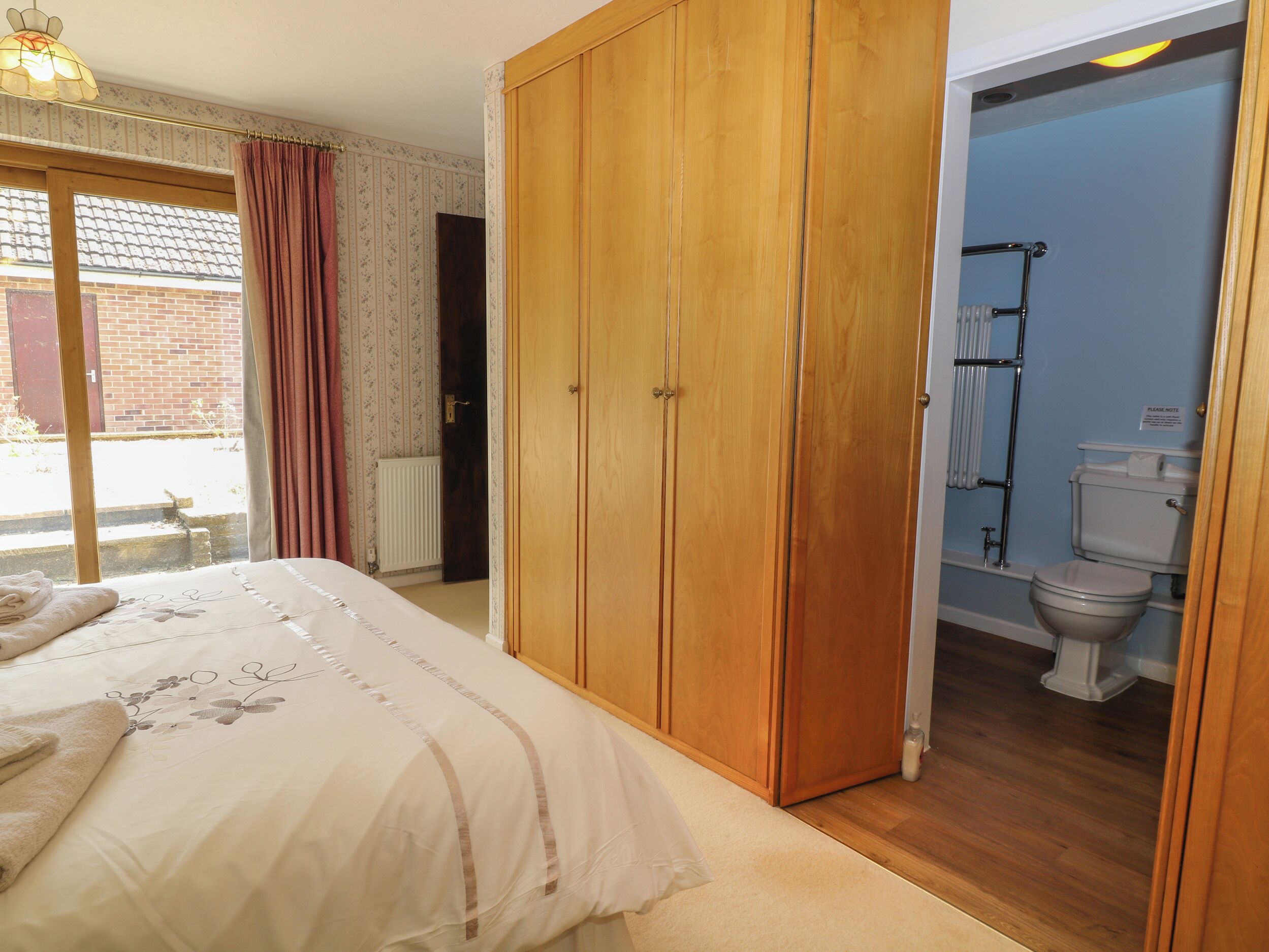 A bedroom with a bed, wooden wardrobe, and a bathroom with a toilet and towel rack.