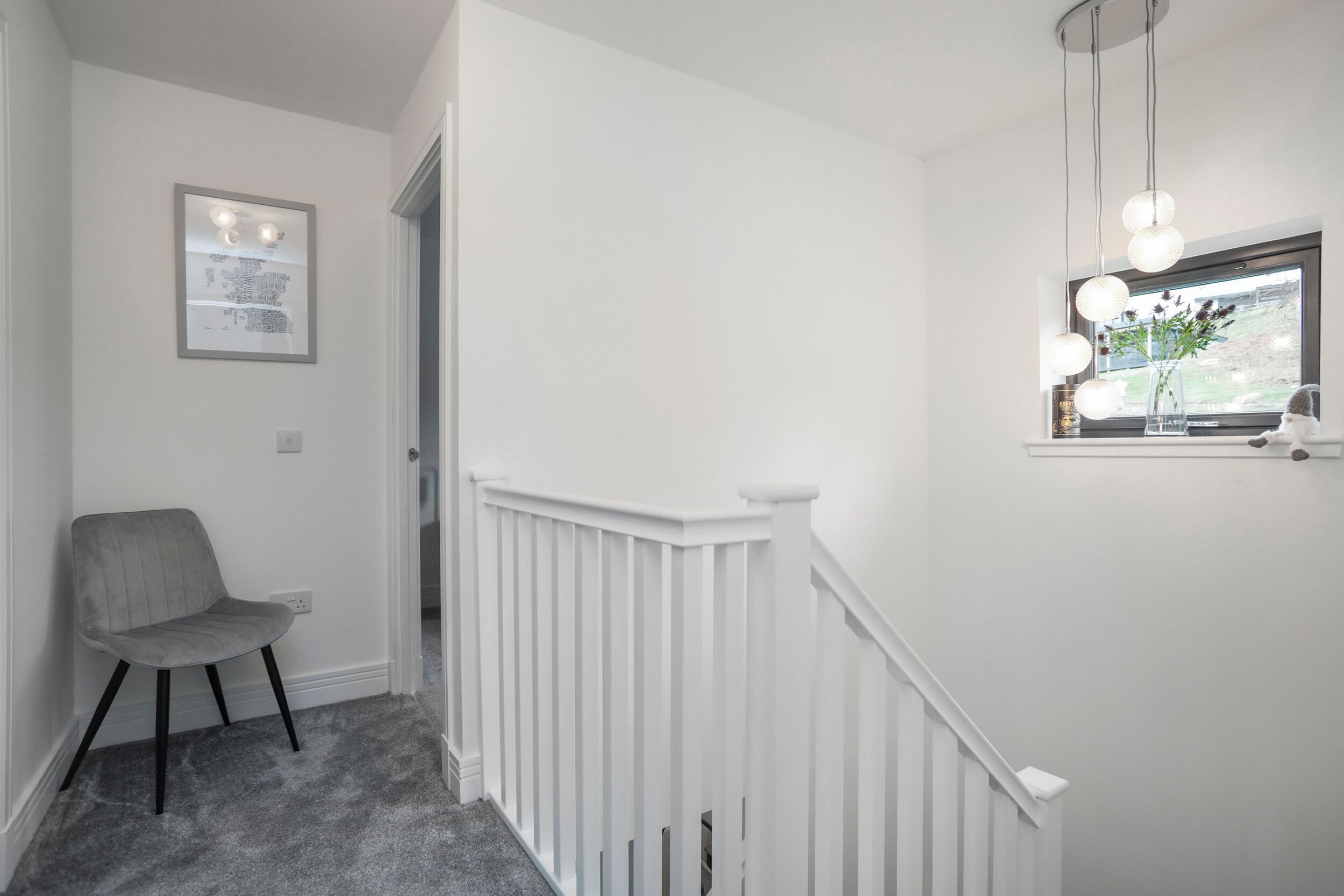 A hallway with a white railing, a gray chair, and a framed picture on the wall.