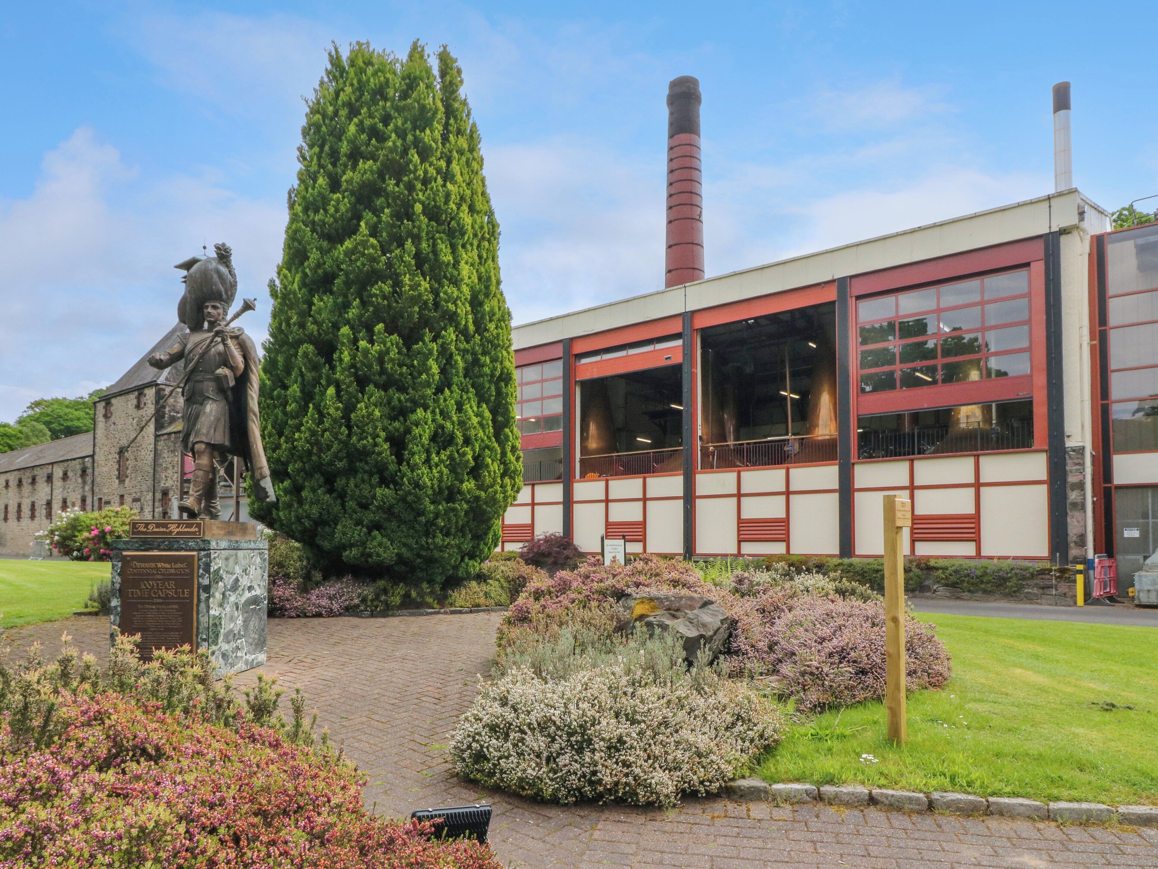 A statue of a soldier, a tall coniferous tree, and a building with large windows and a chimney.