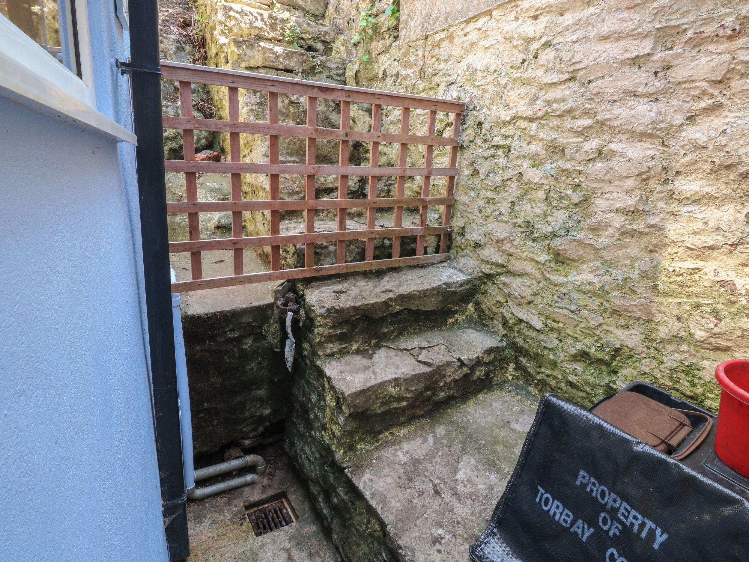 A narrow stone staircase leading to a wooden gate, with a metal pipe and a drain on the steps.