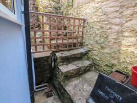 A narrow stone staircase leading to a wooden gate, with a metal pipe and a drain on the steps.