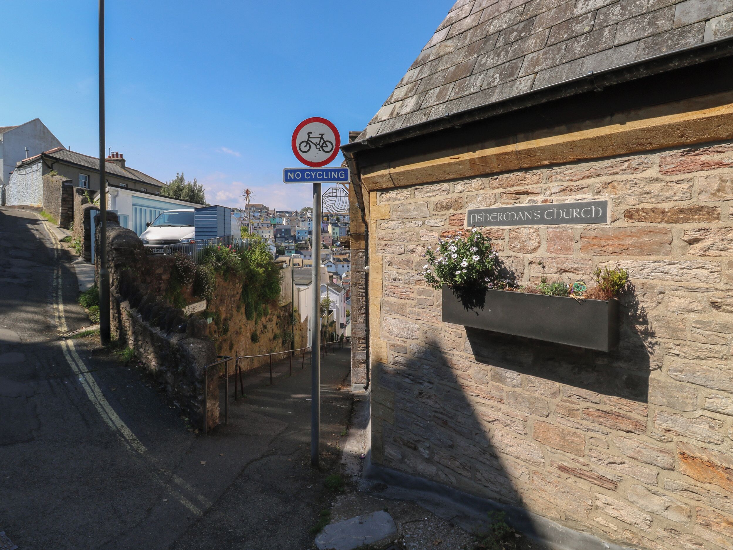 Een verkeersbord dat fietser niet toelaat, en een gebouw met de naam 'Fisher's Church', met stenen muren en een bloemenplanter.