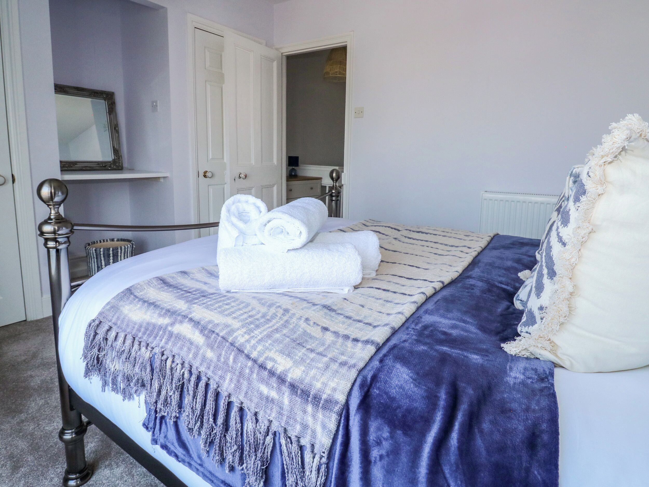 A neatly made bed with a blue and white striped blanket, a rolled white towel, and a white pillow.