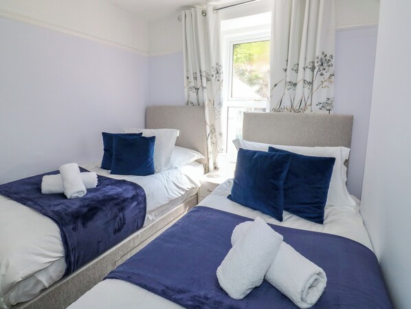 A hotel room with two beds, each with a blue headboard, white bedding, and a blue throw blanket. - Fishnets (Brixham)