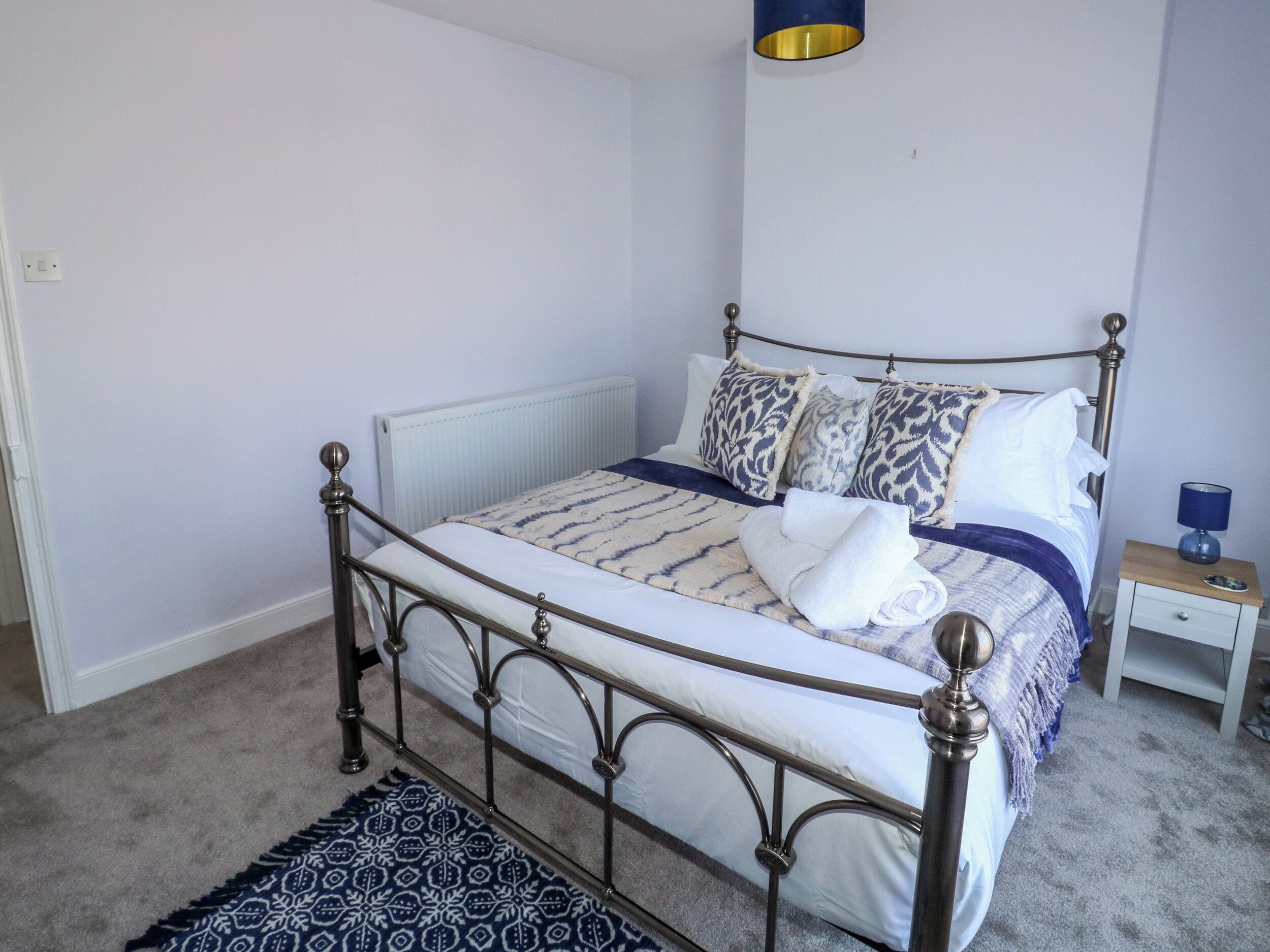 A neatly made bed with patterned bedding, a bedside table with a lamp, and a decorative rug on the floor.