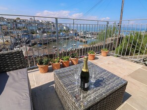 A balcony with a wicker table, potted plants, and a bottle of champagne. - Fishnets (Brixham)