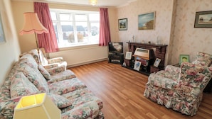 A living room with floral-patterned sofas, a television, a fireplace, and framed pictures on the wall. - Sycamore (Filey)