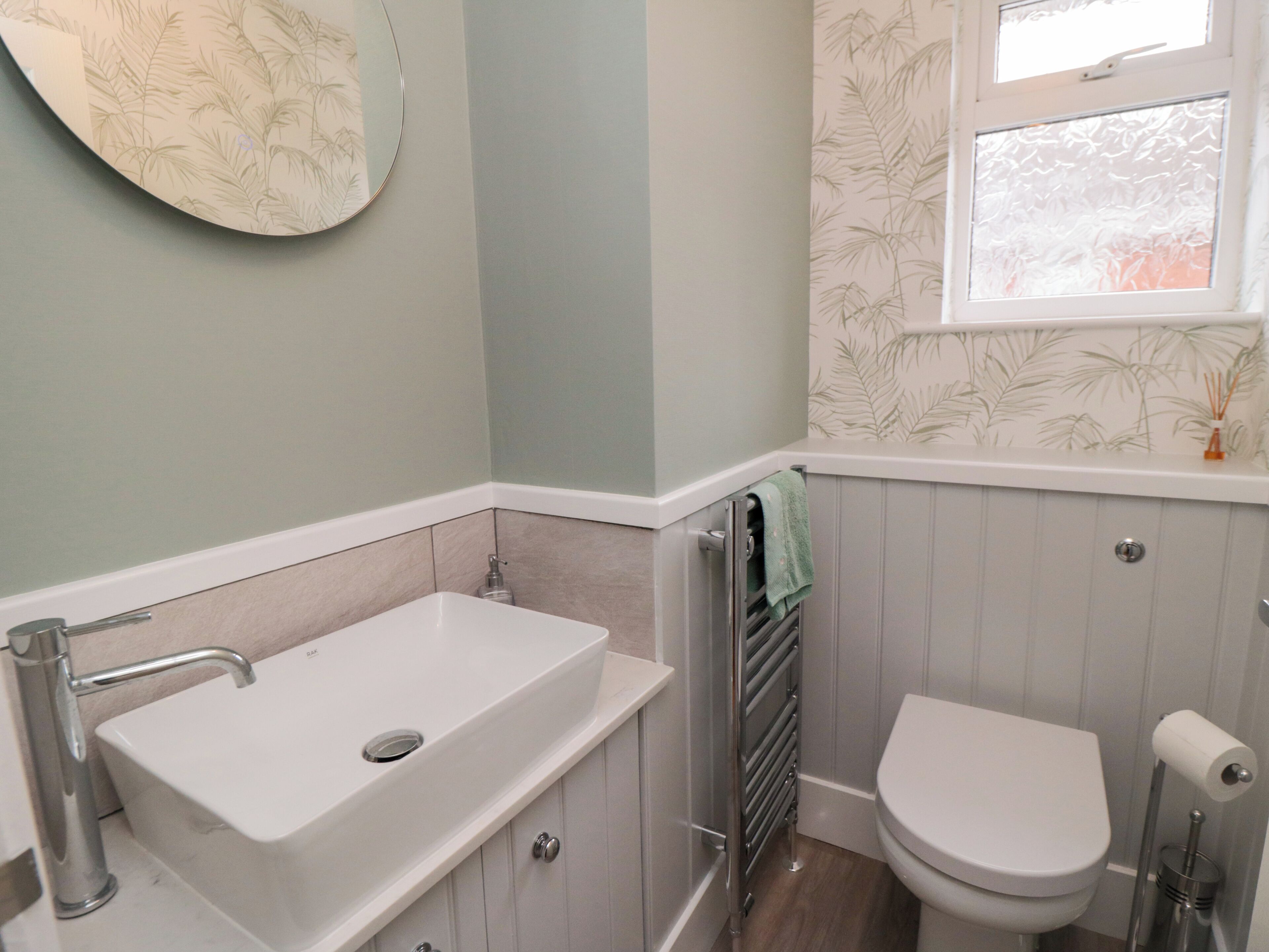 A bathroom with a white sink, toilet, and a window with a leaf-patterned curtain.