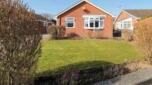 A red brick house with a well-maintained lawn and a small garden area. - Sycamore (Filey)