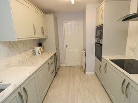 Cocina compacta con armarios de tonos claros, encimera de mármol y placa de inducción negra.