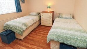 A bedroom with two single beds, a dresser, a lamp, and a window with curtains. - Sycamore (Filey)