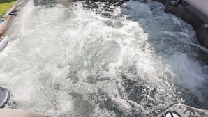 Μια υδρομασάζ με εμφανή χειριστήρια και μια ξύλινη βεράντα στο βάθος.