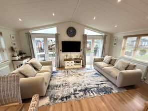 A spacious living room with a large flat-screen TV, two sofas, a coffee table, and a patterned rug. - Lodge 18 - The Pines (Saltburn-by-the-Sea)