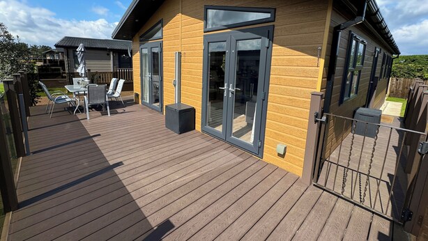 Een modern huis met een houten terras, grote schuifdeuren en een omheind patio.