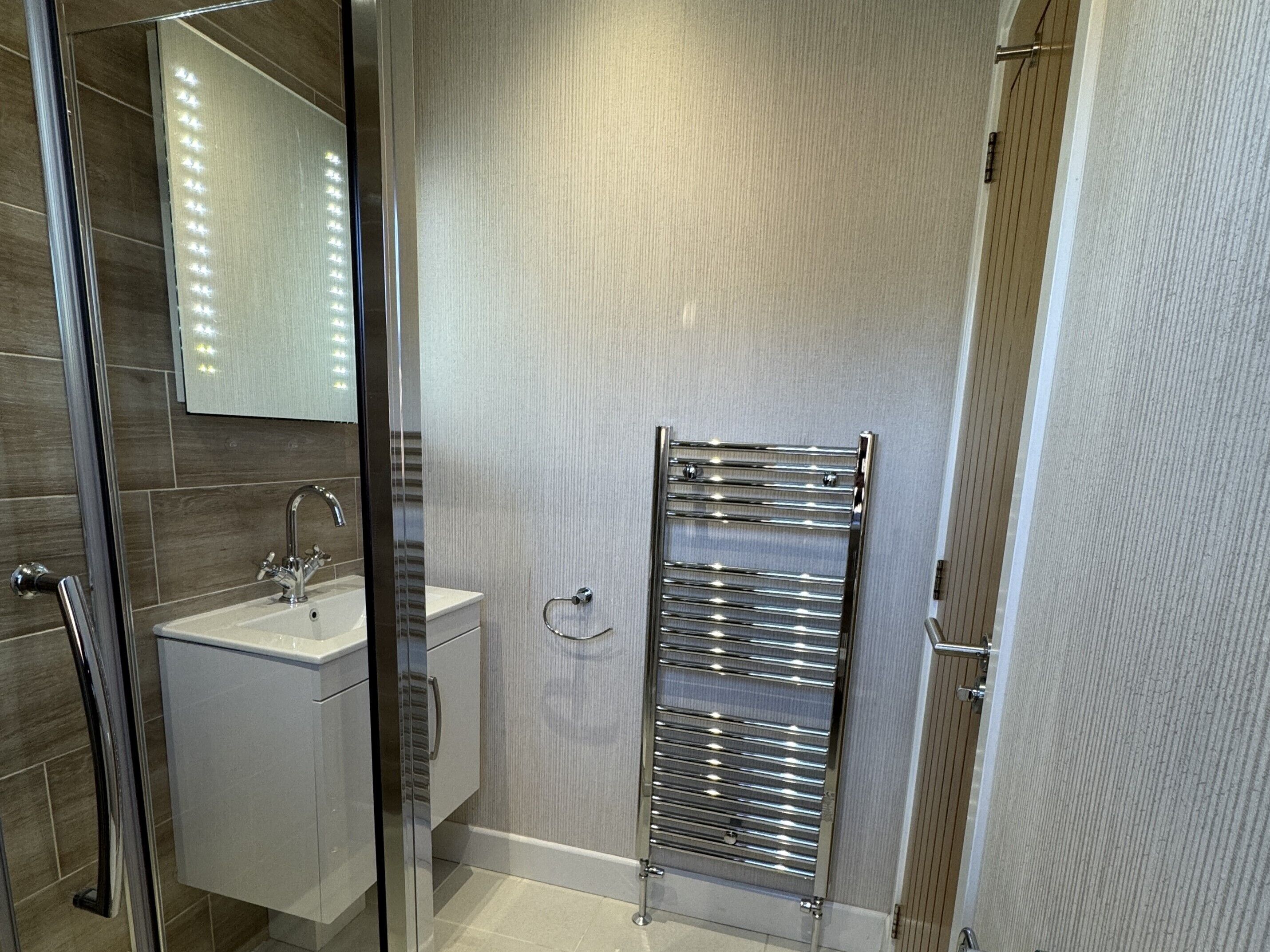 A modern bathroom with a glass shower enclosure, a sink with a chrome faucet, and a towel rack.