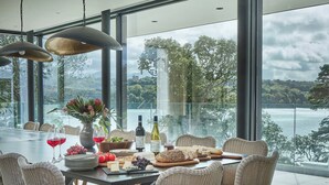 Uma sala de jantar com cadeiras de vime, uma mesa de vidro e vista para um lago.