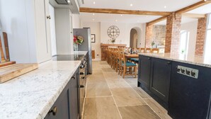 A modern kitchen with a marble countertop, dark cabinetry, and a brick accent wall. - Tanat House (Oswestry)
