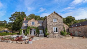 A stone house with a gravel driveway, a front porch, and a small garden area. - Tanat House (Oswestry)