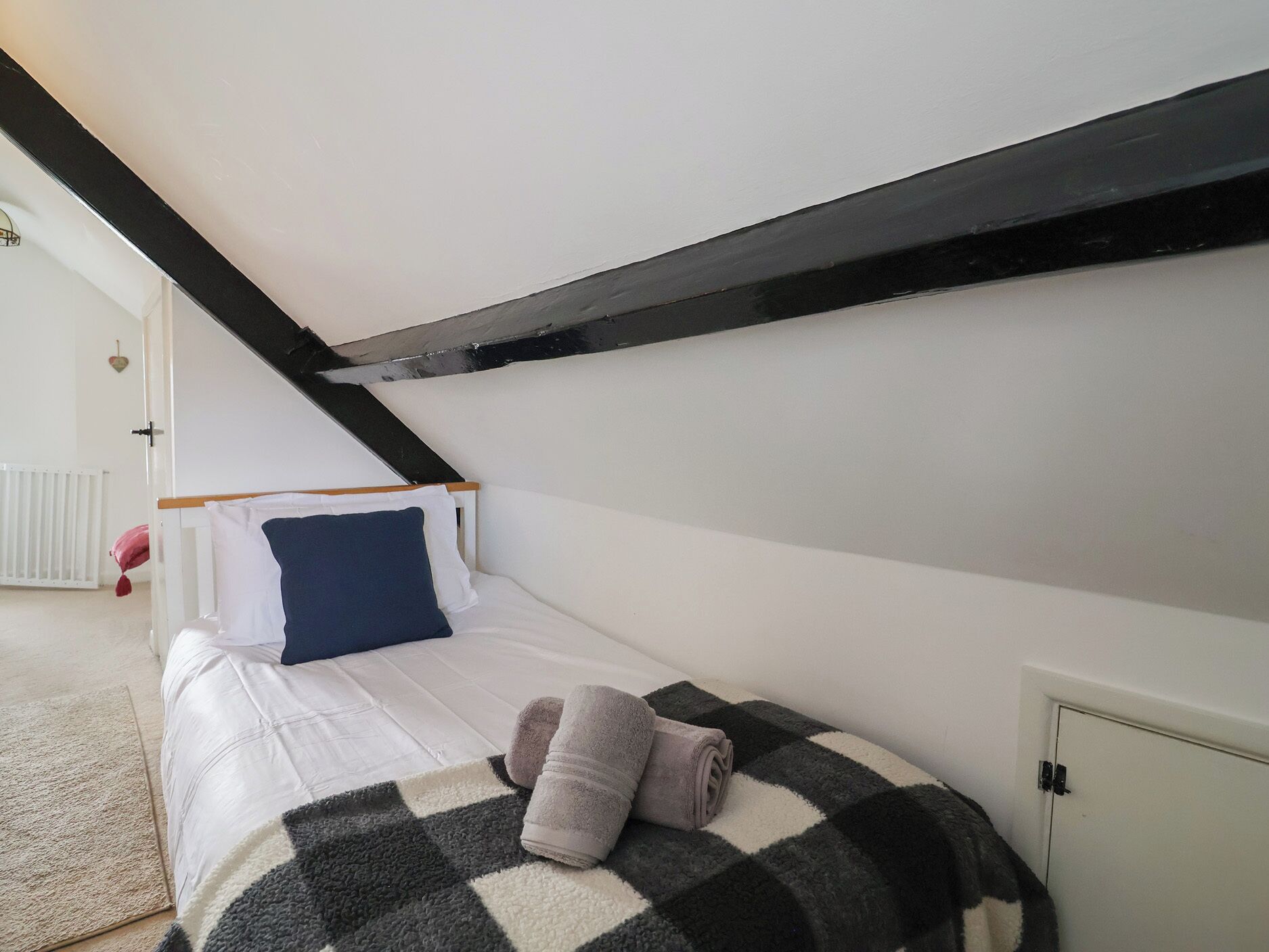 A bedroom with a sloped ceiling, a bed with a checkered blanket, a pillow, and a rolled towel.
